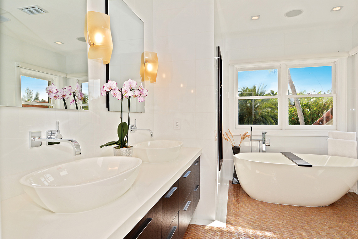 A sleek resort-style master bath that features his-and-hers free-standing sinks, a free-standing tub and a glass shower.Photography: LauderdaleOne Luxury Real Estate.